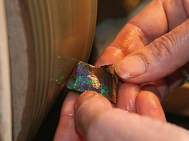 Ein Opalschleifer schleift sorgfältig einen Boulderopal mit Hilfe einer Schleifmaschine.
